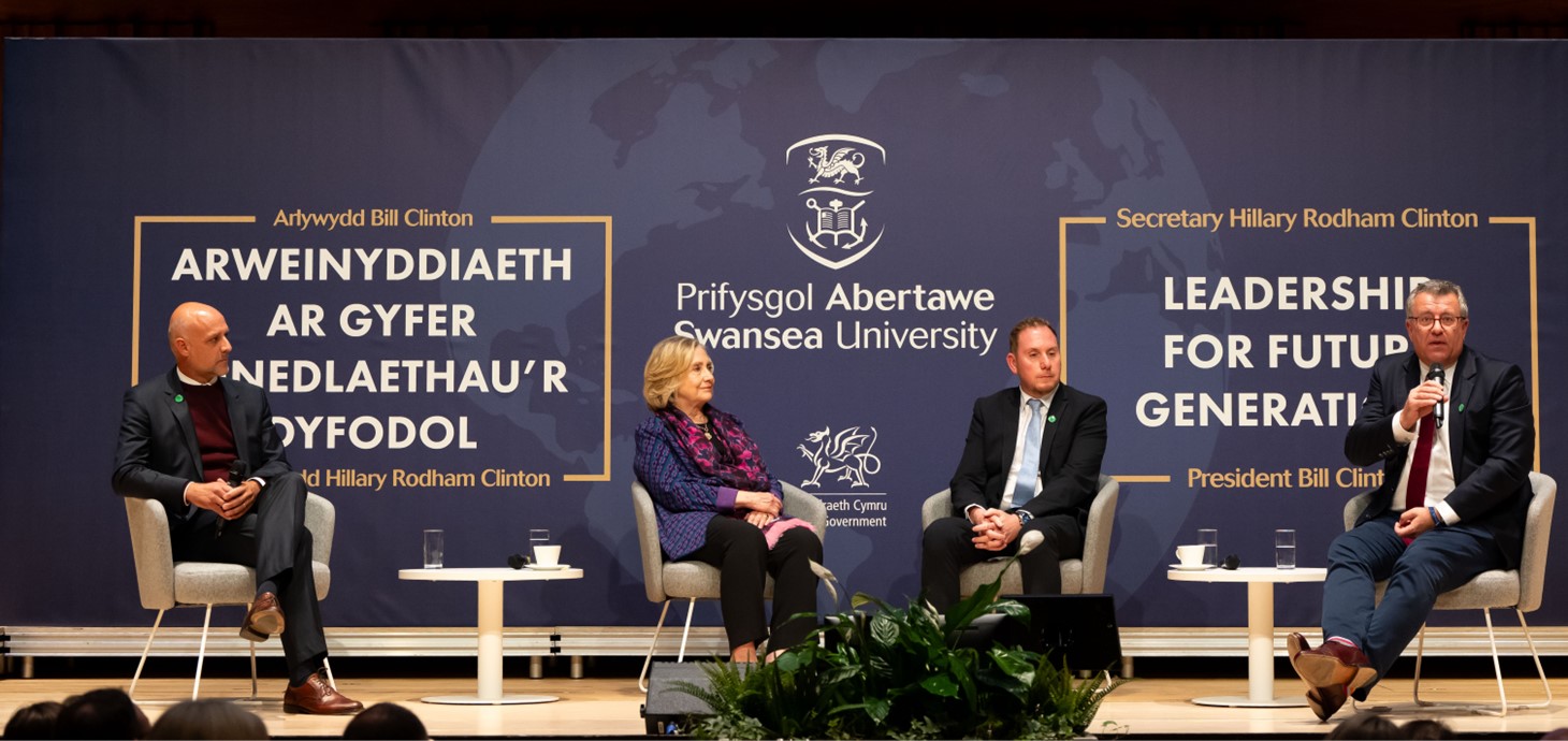 Llun o Nick Gliddon, Cyfarwyddwr Busnes Vodafone, ar y llwyfan yn y digwyddiad gyda'r Ysgrifennydd Hillary Clinton, y Cynghorydd Rob Stewart, Cadeirydd Cyd-bwyllgor Dinas-ranbarth Bae Abertawe, ac Andrea Dona, Cyfarwyddwr Rhwydwaith a Datblygu Vodafone.