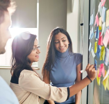 Three members of staff arranging sticky notes on a glass wall